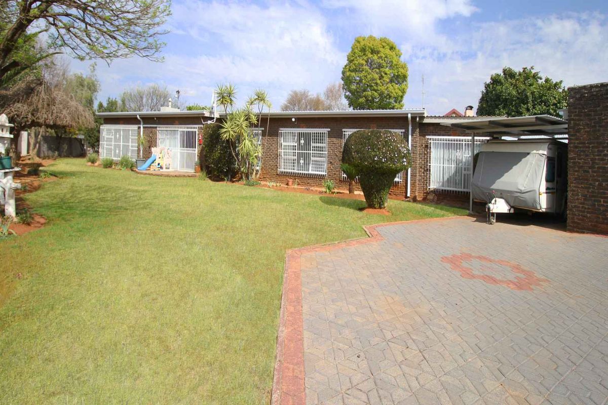 Rear view of the house featuring a brick facade, paved driveway, carport, and a spacious lawn area.