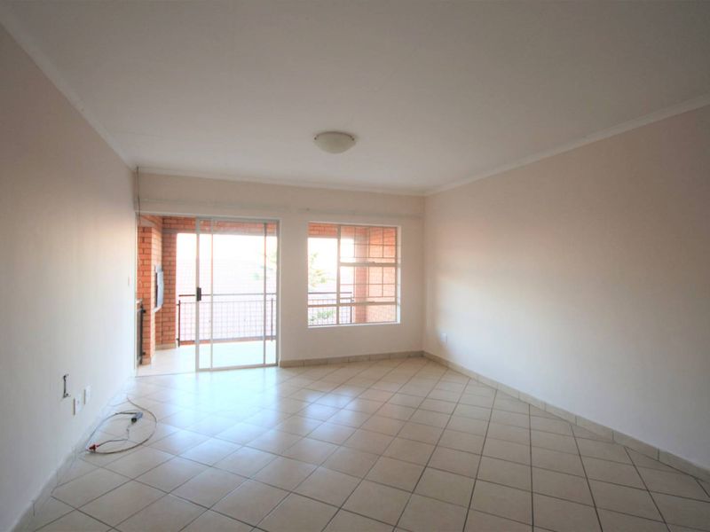 An empty, neutrally painted living room featuring tiled flooring and a sliding glass door providing access to an outdoor balcony area.