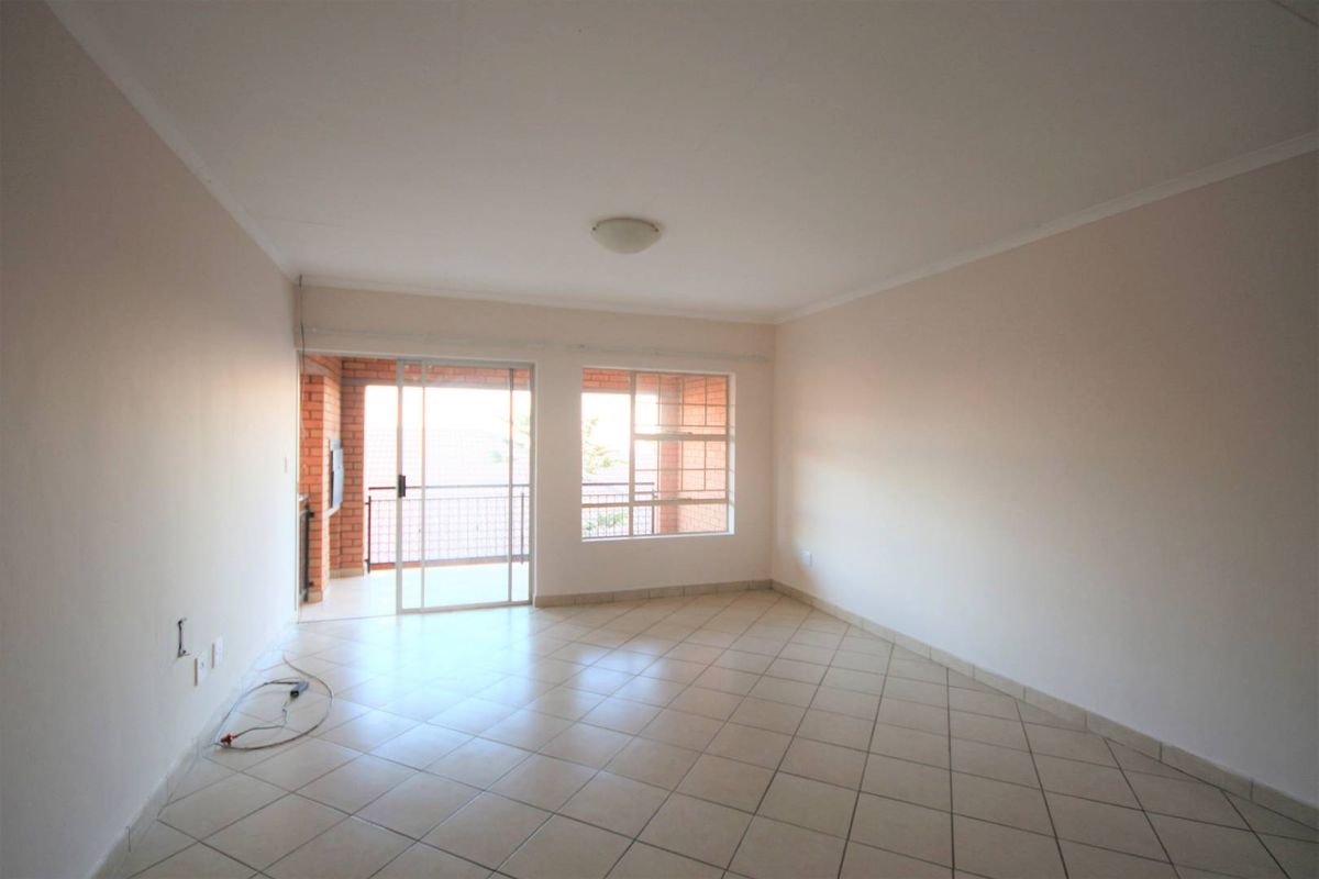 An empty, neutrally painted living room featuring tiled flooring and a sliding glass door providing access to an outdoor balcony area.