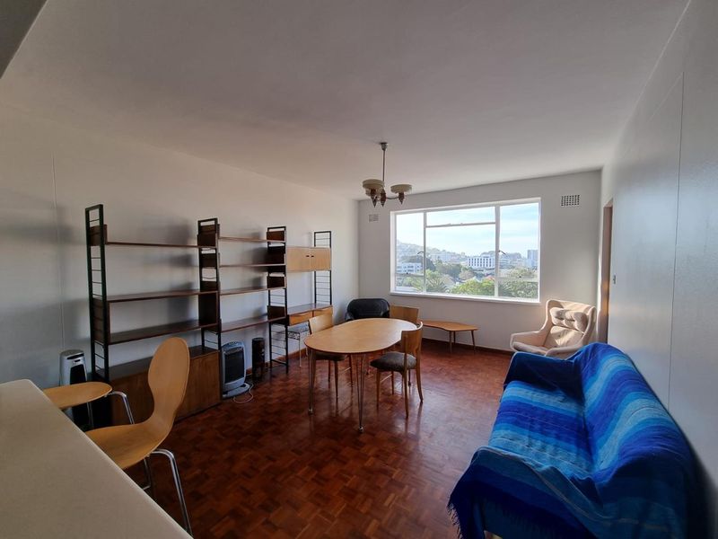 Spacious living room featuring original parquet flooring, large window with city views, and neutral wall finishes, offering a bright and versatile living space.