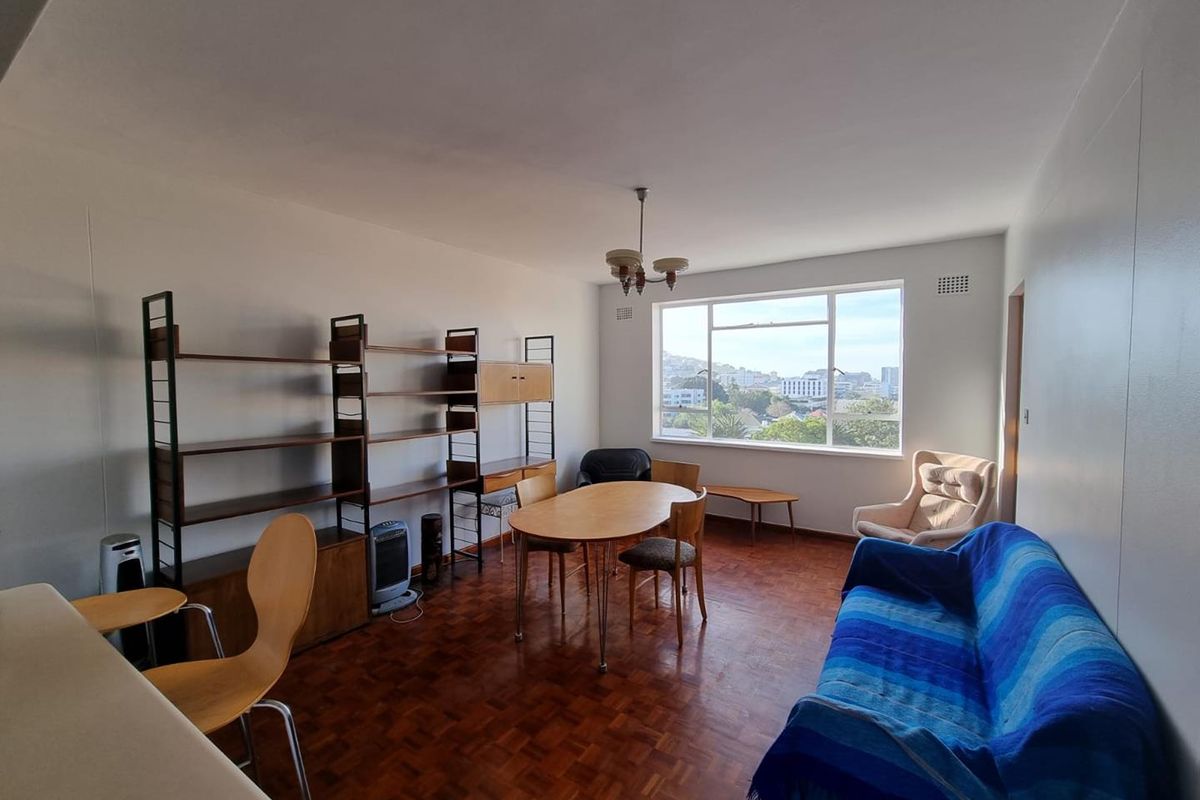 Spacious living room featuring original parquet flooring, large window with city views, and neutral wall finishes, offering a bright and versatile living space.