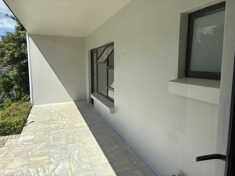 A clean, covered patio area featuring neutral tiled flooring and modern aluminium window frames, offering a bright and well-maintained outdoor space.