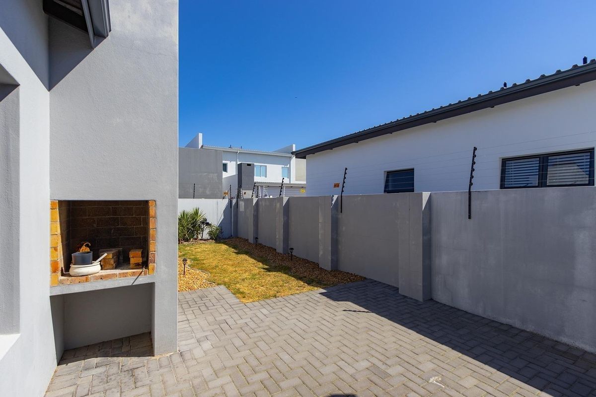A private rear courtyard featuring a built-in brick braai, paved patio area, and a small low-maintenance garden enclosed by perimeter walls.