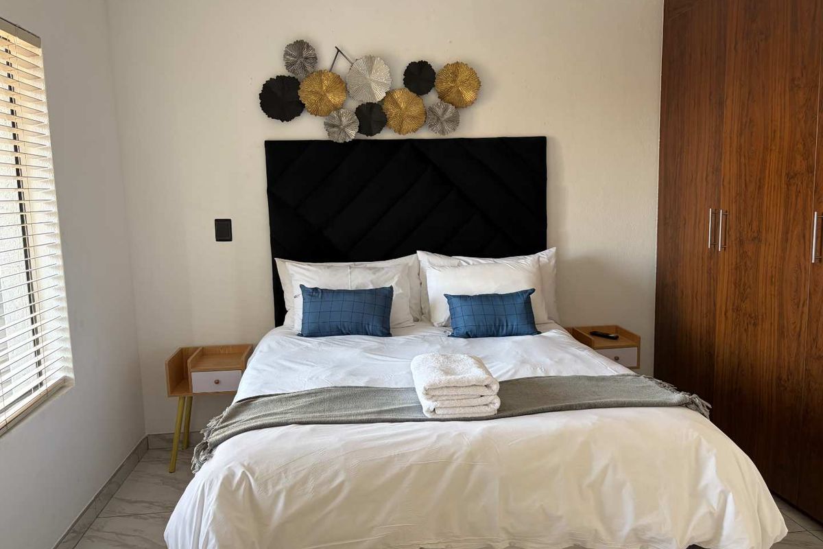 A well-maintained bedroom featuring built-in wooden cupboards, tiled flooring, and venetian blinds, offering a clean and functional living space.