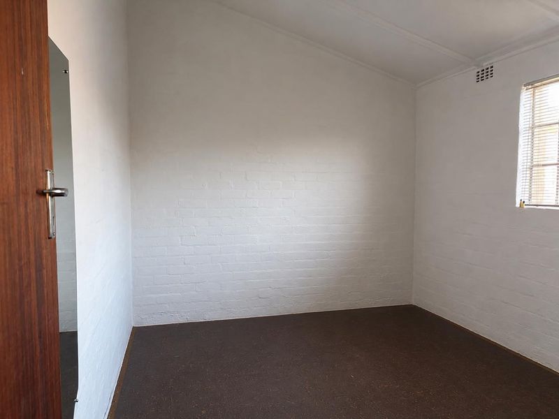A clean, empty bedroom featuring painted brick walls, a sloped ceiling, and a window with fitted blinds.