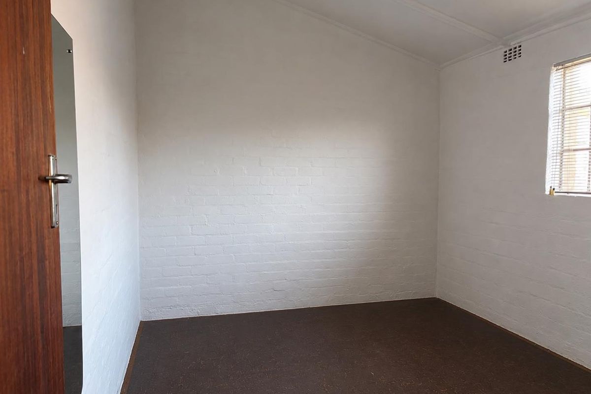 A clean, empty bedroom featuring painted brick walls, a sloped ceiling, and a window with fitted blinds.