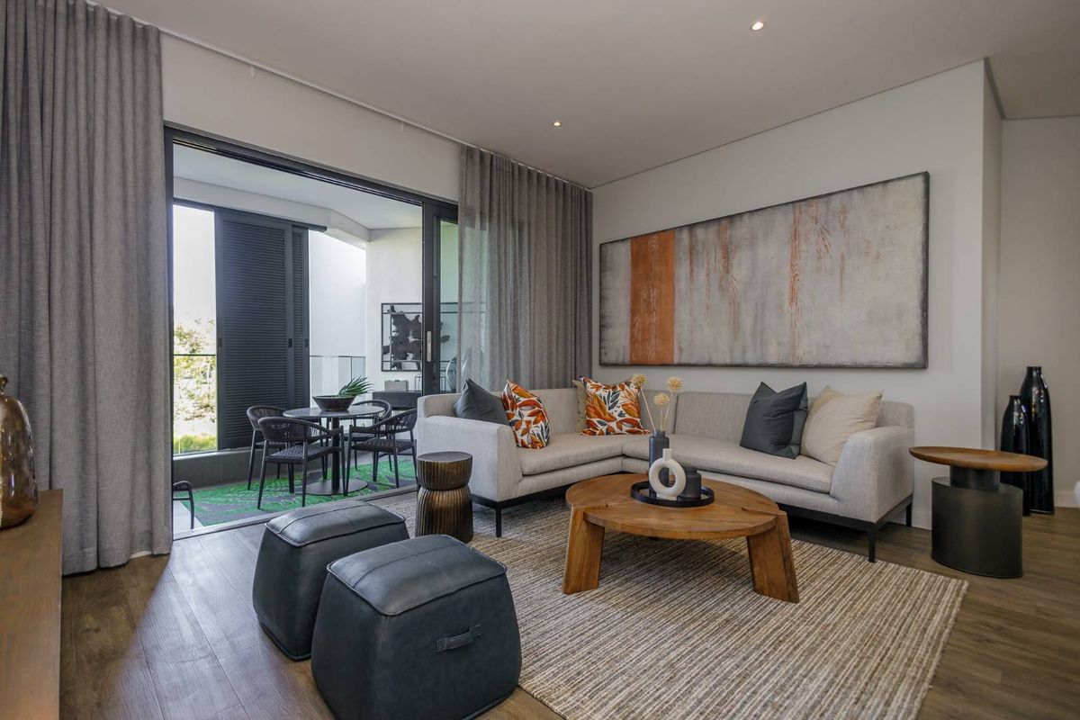 Modern living room featuring timber flooring, recessed downlighting, and large sliding glass doors providing seamless access to a private balcony.