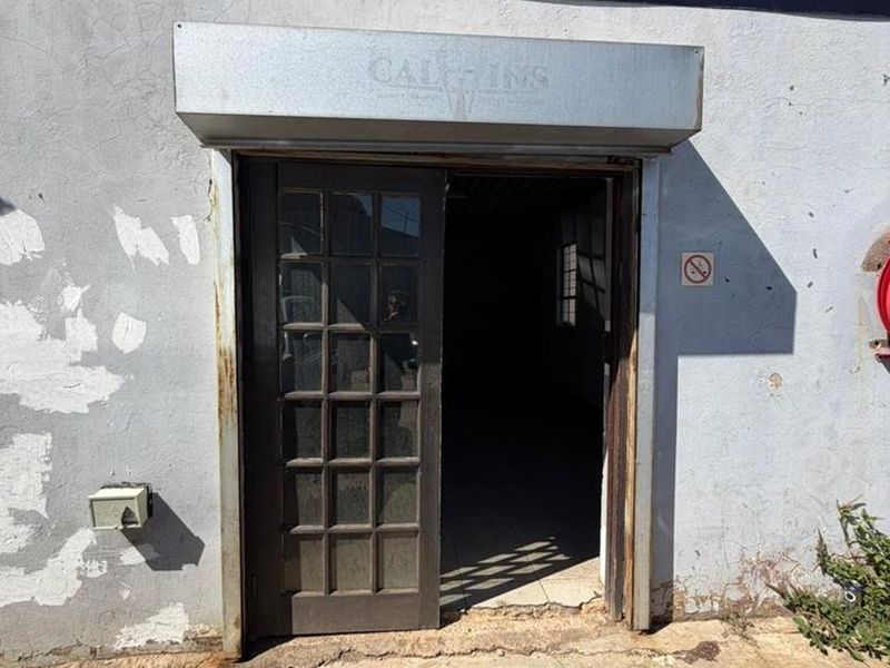 Front entrance of a commercial unit featuring a glass-paneled door, roller shutter housing, and weathered exterior wall finish.