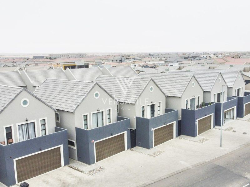Aerial view of a row of modern townhouses featuring tiled roofs, integrated garages, and upper-level balconies in a residential estate.