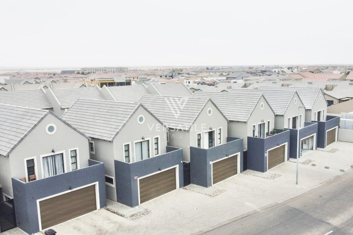 Aerial view of a row of modern townhouses featuring tiled roofs, integrated garages, and upper-level balconies in a residential estate.