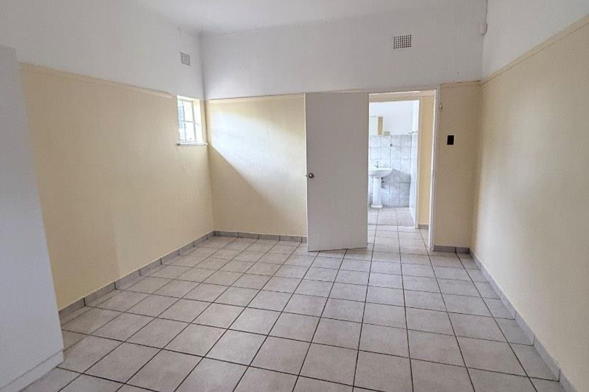 An empty bedroom featuring tiled flooring and half-height wall paneling, with an adjacent bathroom visible through the doorway.