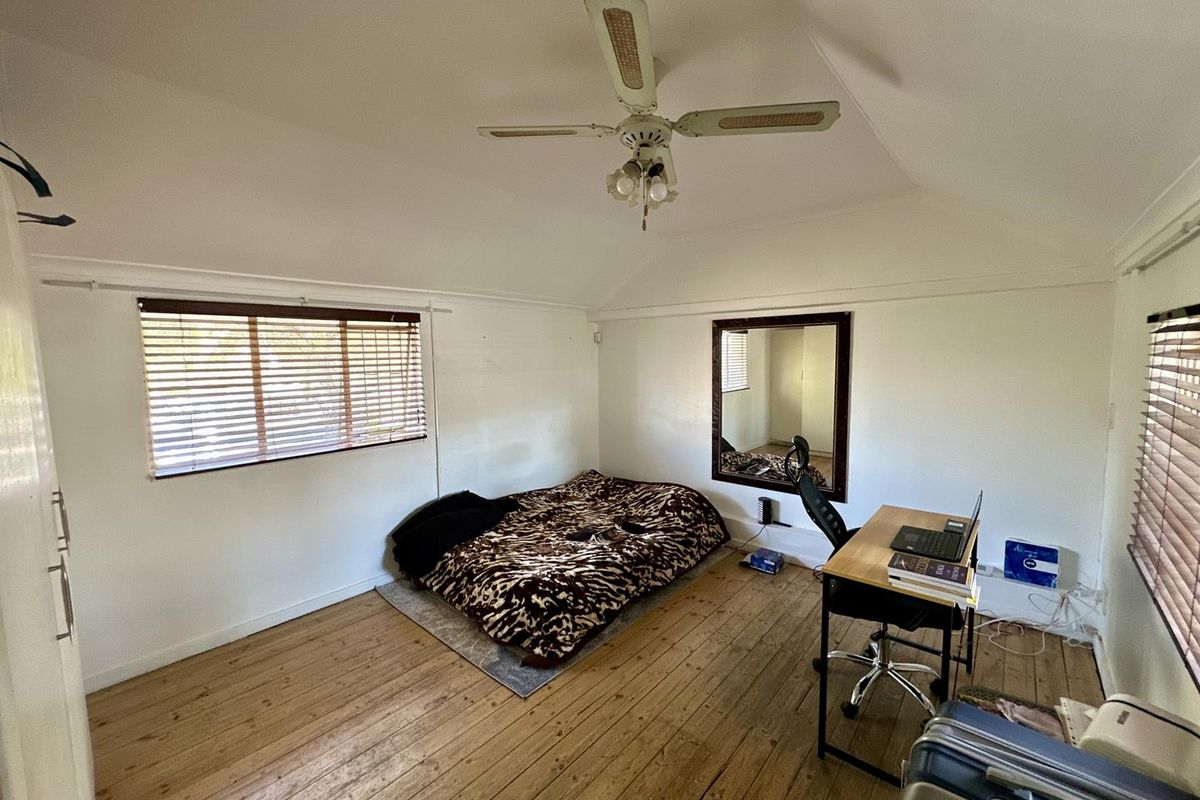 A bedroom featuring timber flooring, a ceiling fan, and venetian blinds, offering a functional space with natural light.
