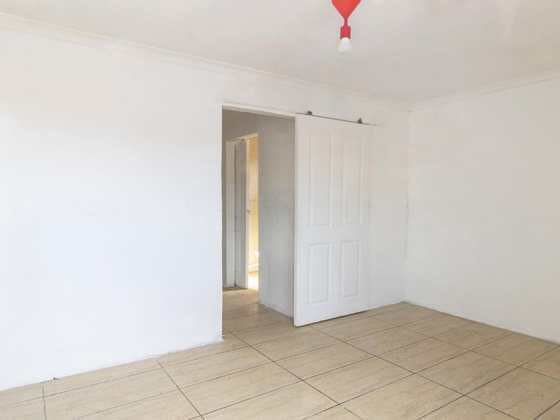 An empty bedroom featuring ceramic floor tiles, a sliding door, and a coved ceiling, presenting a blank canvas for renovation or staging.