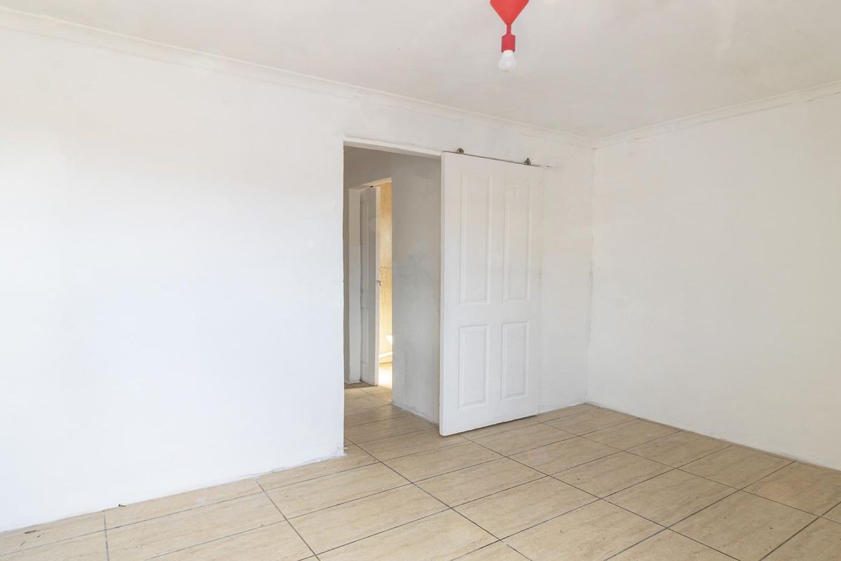 An empty bedroom featuring ceramic floor tiles, a sliding door, and a coved ceiling, presenting a blank canvas for renovation or staging.