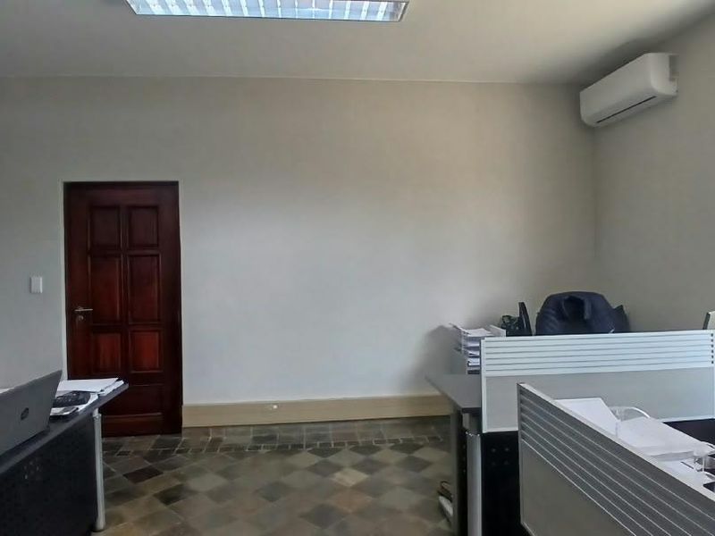 A functional office space featuring tiled flooring, an integrated air conditioning unit, and secure window bars, providing a practical work environment.