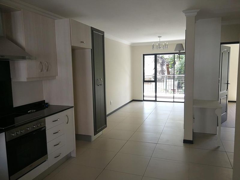 An open-plan kitchen and living area featuring modern cabinetry, tiled floors, and a sliding door leading to a balcony.