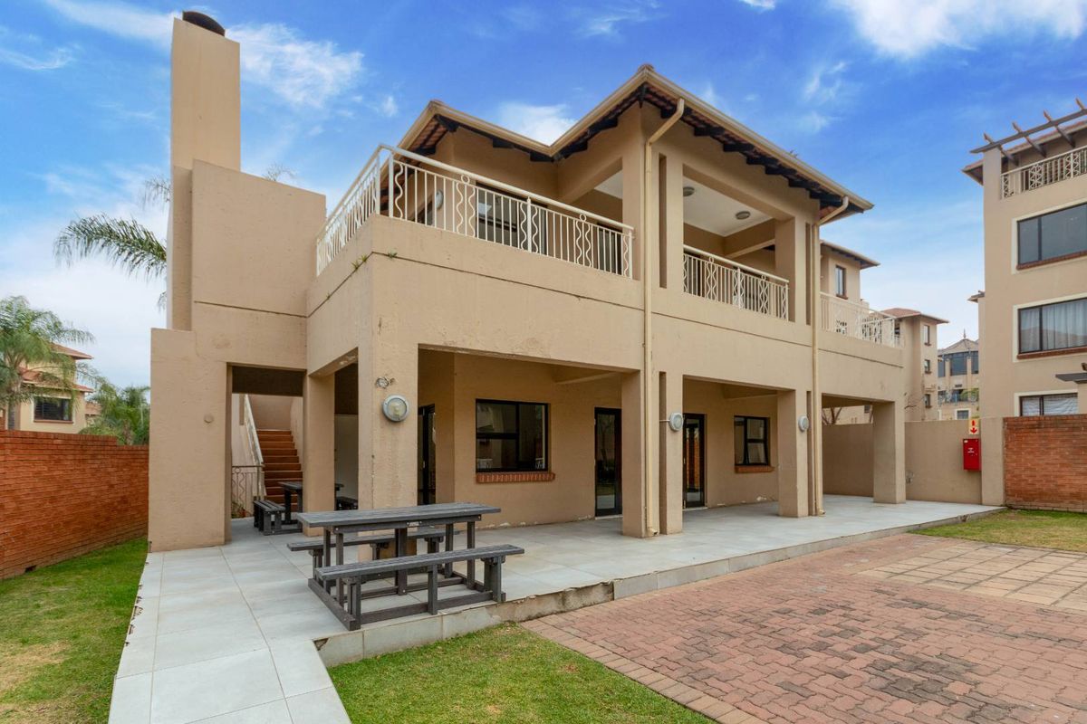 Rear view of a multi-story apartment building featuring a covered ground-floor patio, an upper-level balcony with metal railings, and an external staircase.