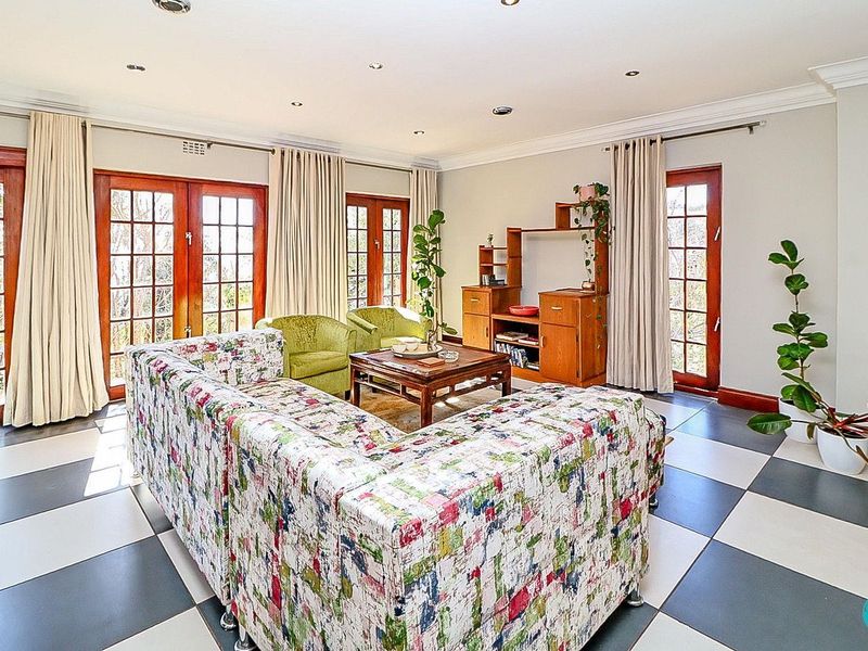 Spacious living room featuring large checkered floor tiles, recessed lighting, crown molding, and multiple sets of wooden french doors providing natural light.