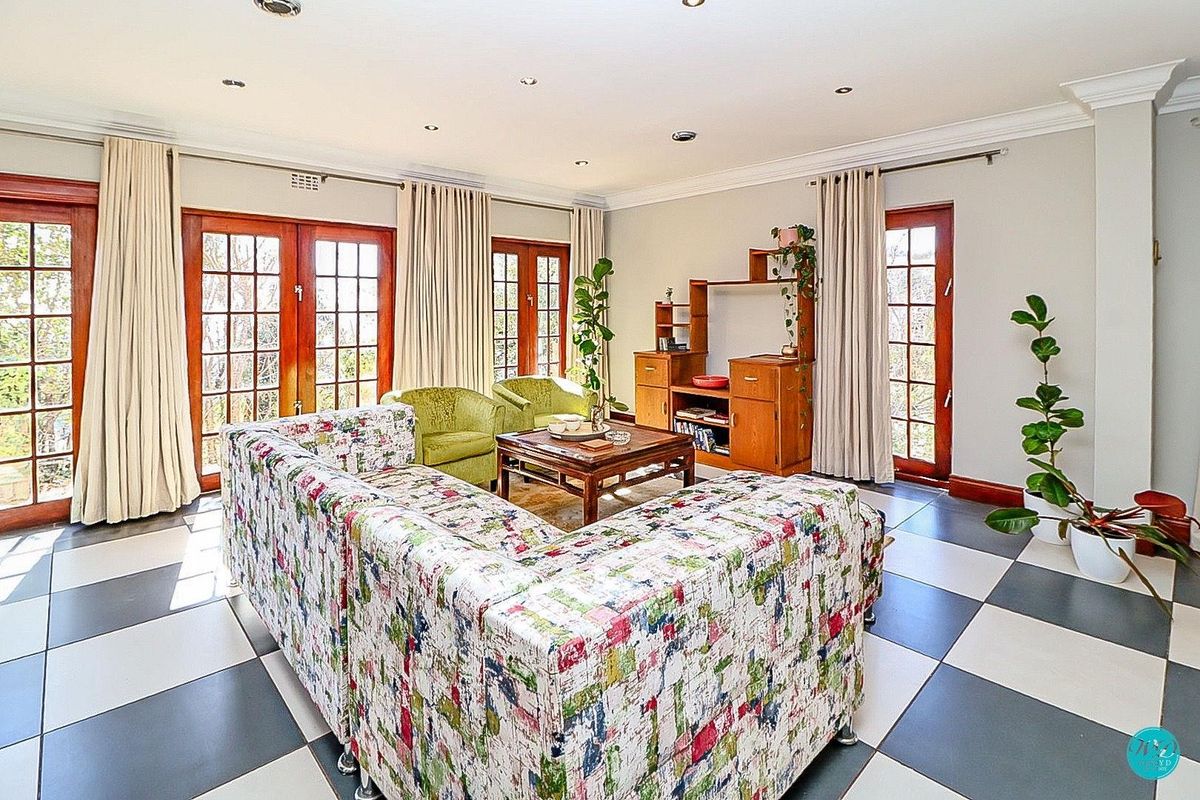 Spacious living room featuring large checkered floor tiles, recessed lighting, crown molding, and multiple sets of wooden french doors providing natural light.