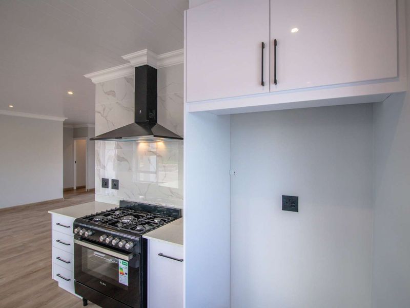 Modern kitchen featuring a gas stove, extractor fan, marble-look splashback, and ample built-in cabinetry with stone countertops.