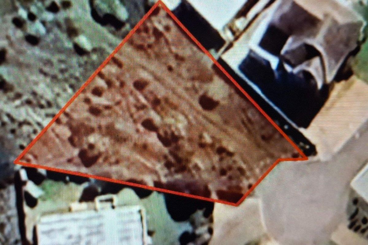 An aerial view of a vacant residential plot outlined in red, showing the land parcel in relation to surrounding properties.
