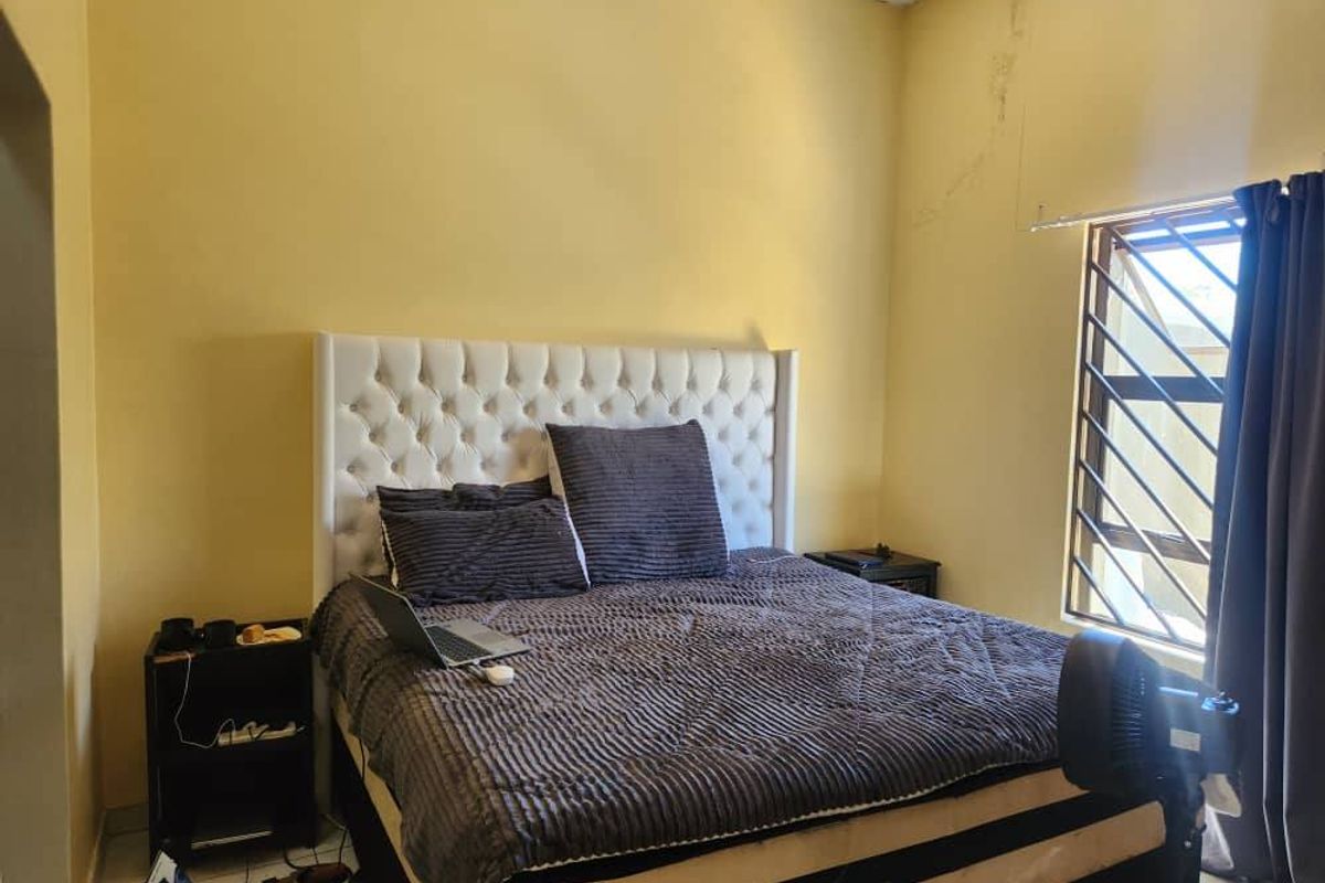 A bedroom featuring a window with security bars and yellow painted walls showing signs of water damage.