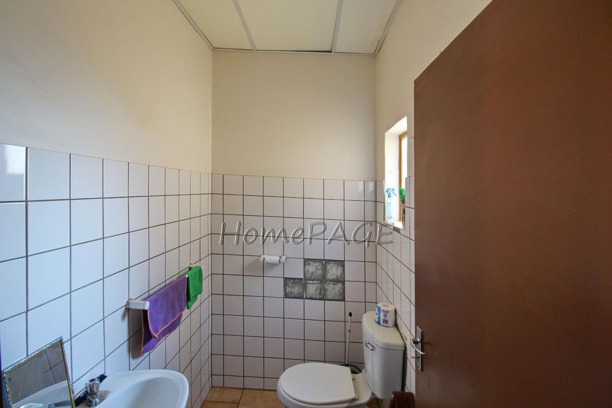 A functional bathroom featuring a standard toilet, wall-mounted basin, and partial wall tiling with visible areas requiring maintenance.