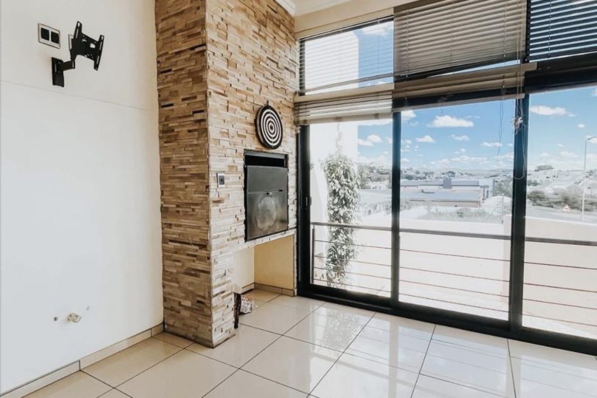 Bright living area featuring large sliding glass doors, polished floor tiles, and a prominent stone-clad built-in fireplace.