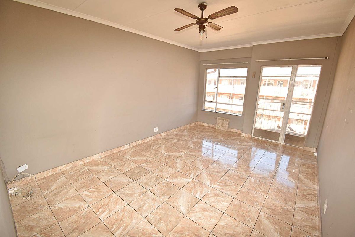 An empty living room featuring tiled flooring, a ceiling fan, and access to a balcony through a glass door.