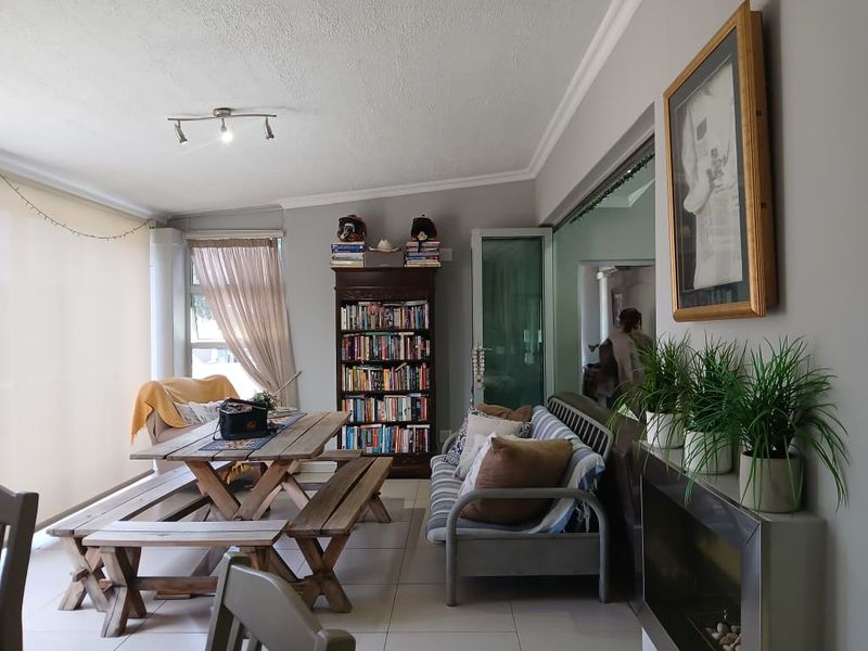 A spacious living area featuring tiled flooring, a built-in fireplace, and large windows with roller blinds, offering a comfortable and functional layout.