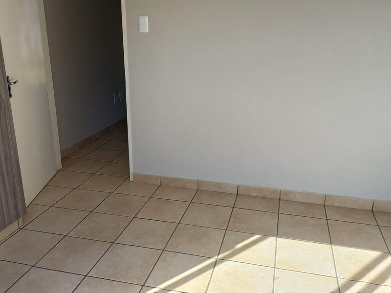 An empty bedroom featuring neutral tiled flooring, built-in cupboard storage, and clean wall finishes, providing a blank canvas for personalization.