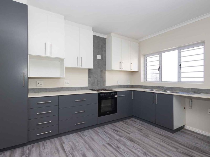 Modern kitchen featuring two-tone cabinetry, stone countertops, built-in oven and hob, tiled splashback, and durable laminate flooring.