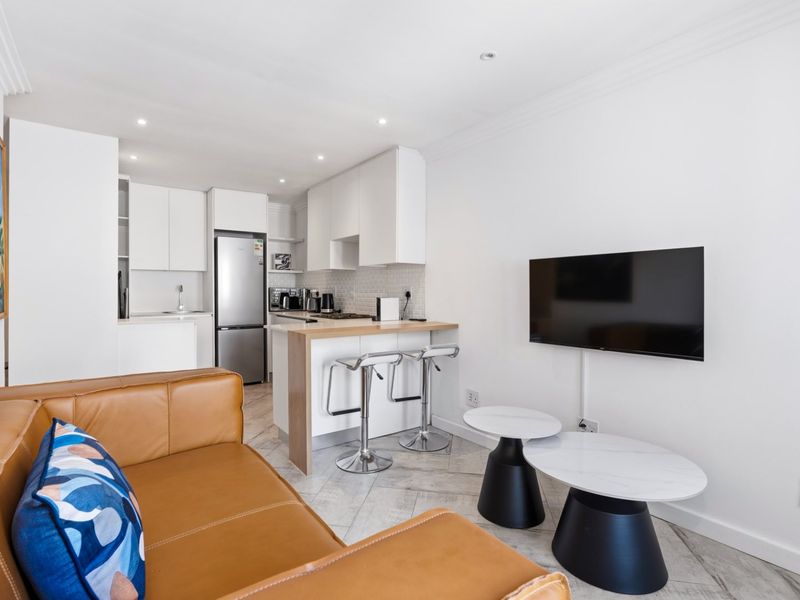 Modern open-plan living area featuring a compact kitchen with built-in cabinetry, a breakfast island, and tiled flooring throughout.