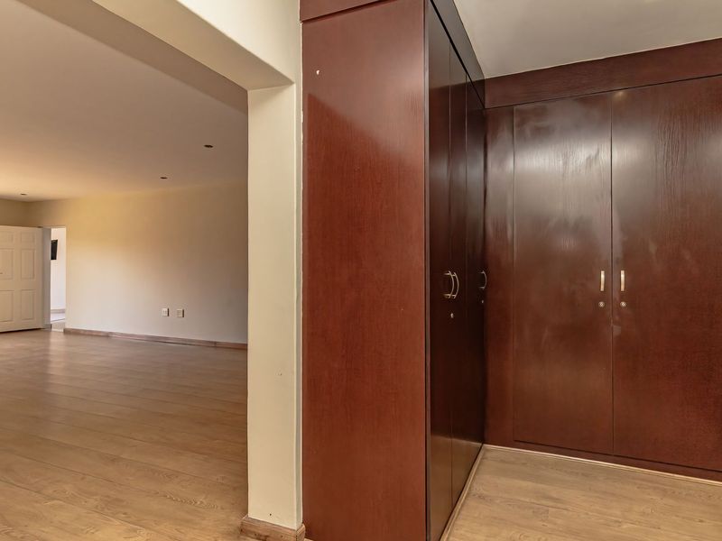 Spacious bedroom featuring extensive dark wood built-in cupboards and modern laminate flooring, offering a clean and neutral canvas for personalization.