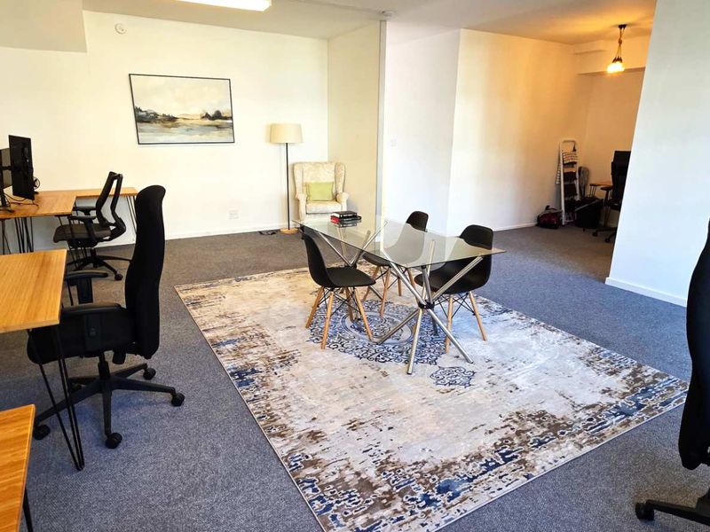 A spacious, open-plan office area featuring neutral walls, carpeted flooring, and multiple workstations, suitable for a collaborative professional environment.