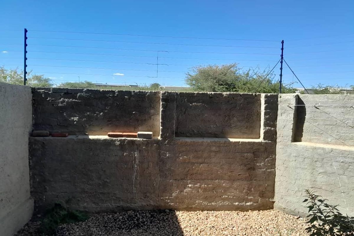 A rear outdoor area featuring a masonry boundary wall with integrated electric fencing and gravel ground cover, requiring maintenance and finishing.