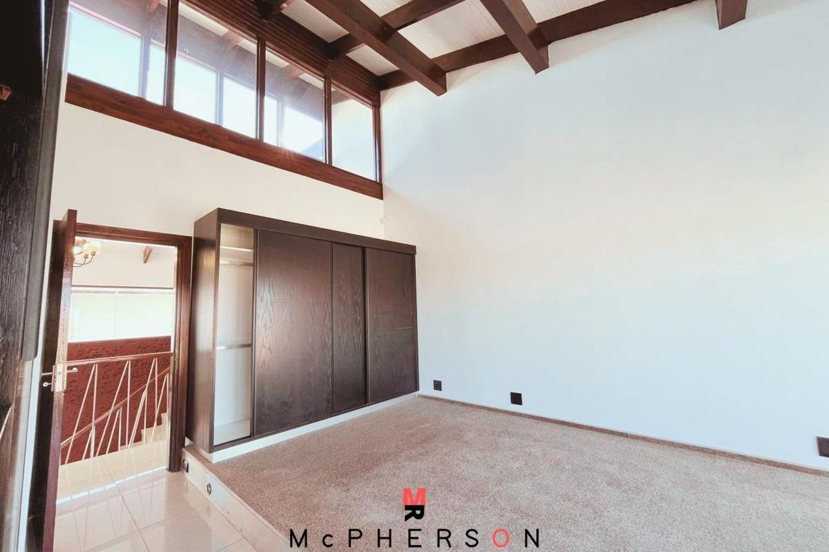 Spacious bedroom featuring high vaulted ceilings with exposed timber beams, large clerestory windows, and built-in dark wood cabinetry.