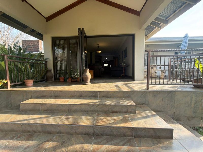 A spacious covered patio featuring tiled steps, wrought iron railings, and exposed timber beams, providing seamless indoor-outdoor flow through bi-fold doors.