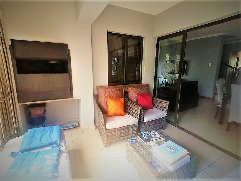 Covered patio area featuring a built-in braai, tiled flooring, and sliding glass doors providing seamless access to the interior living space.