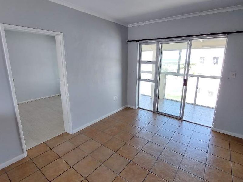 An empty living room featuring tiled flooring and a sliding glass door providing access to an outdoor balcony area.