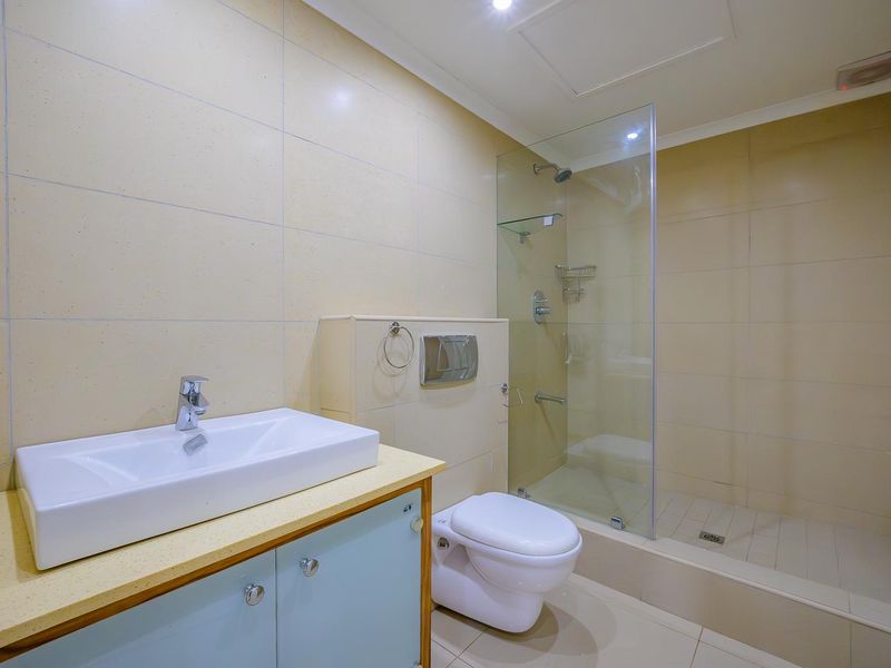 A clean, modern bathroom featuring a wall-mounted toilet, glass-enclosed shower, and a vanity unit with a countertop basin.
