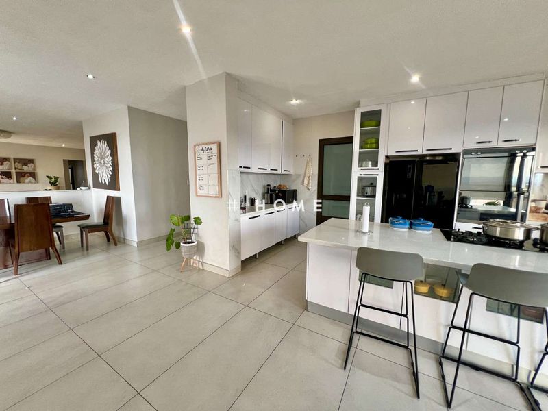 Modern open-plan kitchen and dining area featuring sleek white cabinetry, stone countertops, integrated appliances, and large format floor tiles.