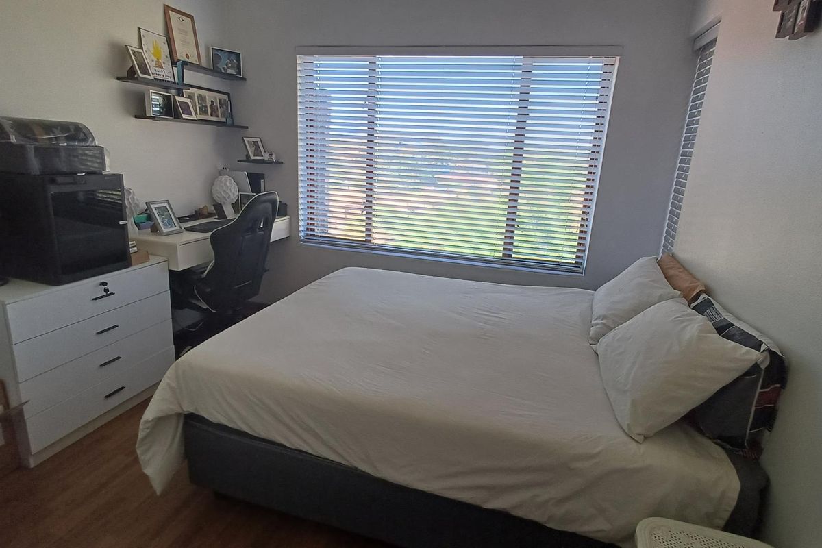 A functional bedroom featuring laminate flooring and large windows fitted with venetian blinds, offering natural light and exterior views.