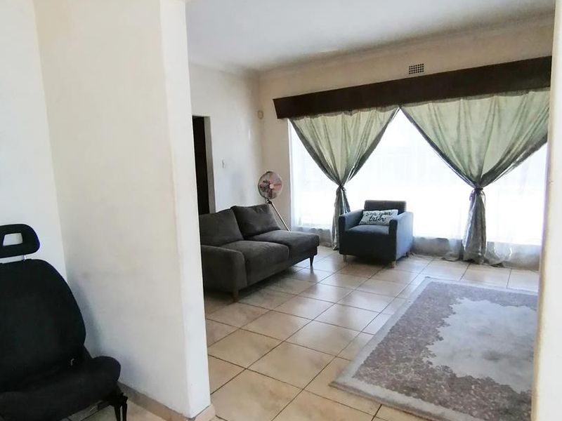 A living room area featuring neutral ceramic floor tiles, a large window with a pelmet, and an open-plan layout connecting to adjacent spaces.