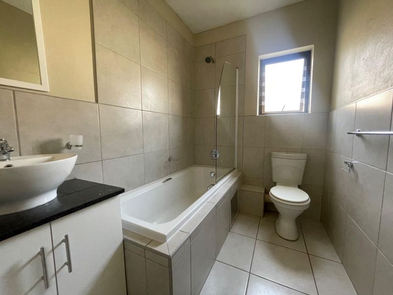 A functional bathroom featuring a vessel sink on a granite vanity, a bathtub with a glass shower screen, and neutral wall and floor tiling.