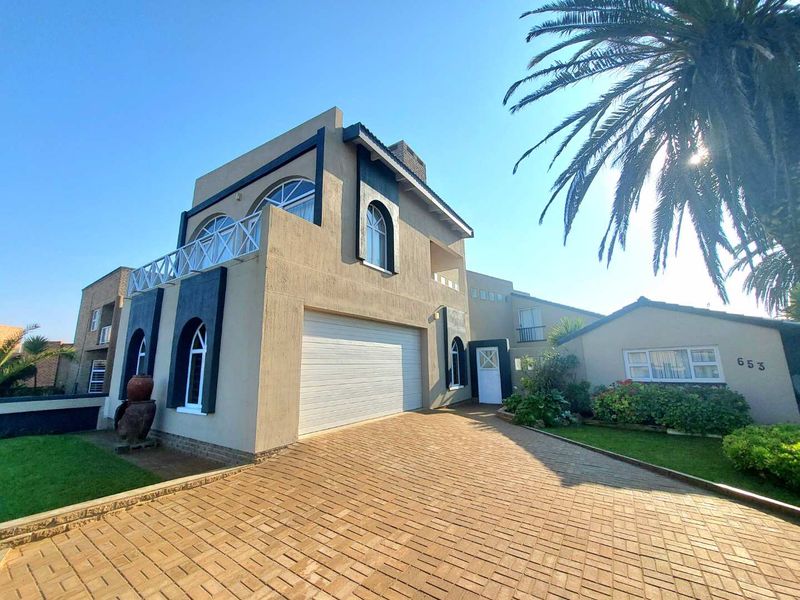 Front elevation of a two-story house featuring a paved driveway, double garage, arched windows, and a balcony, set within a landscaped garden.