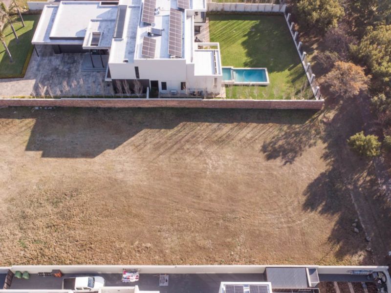 Aerial view of a vacant residential plot situated in a developed estate, offering a clear building footprint adjacent to existing luxury homes.