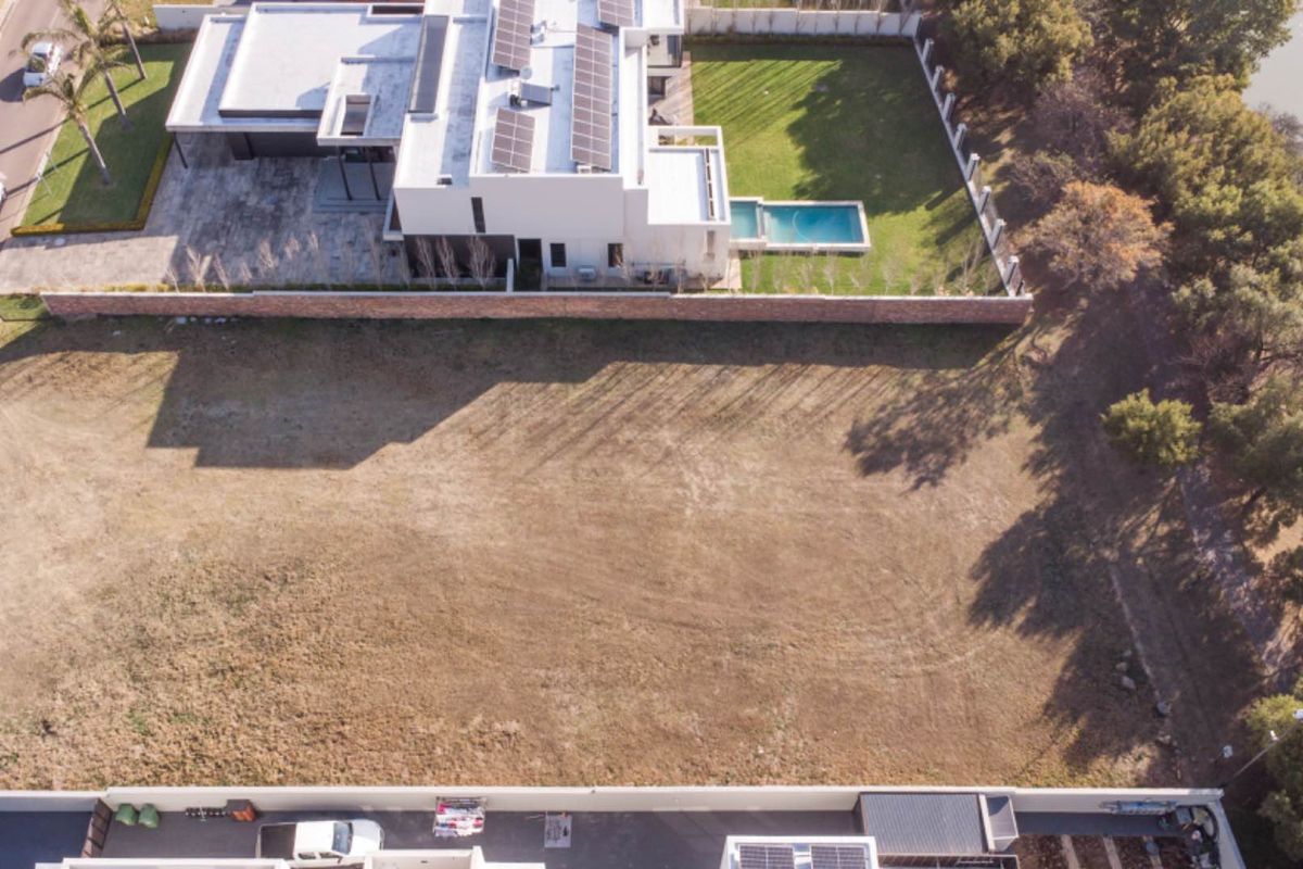 Aerial view of a vacant residential plot situated in a developed estate, offering a clear building footprint adjacent to existing luxury homes.
