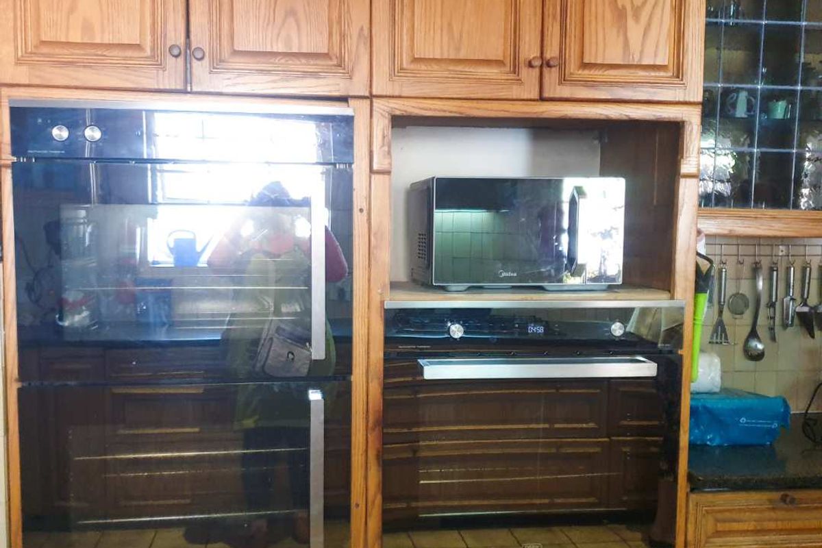 A kitchen wall featuring built-in ovens, a microwave, and traditional wooden cabinetry with granite countertops.