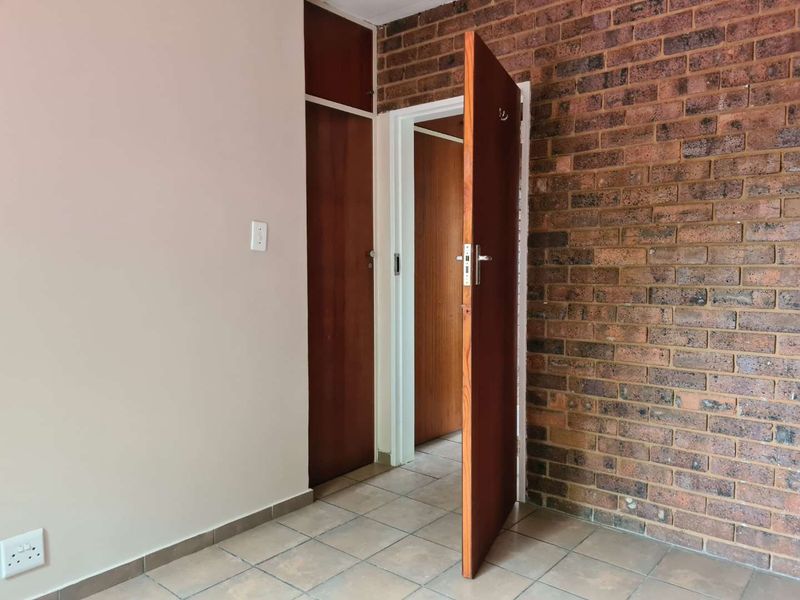 An empty bedroom featuring an exposed brick feature wall, tiled flooring, and a built-in wooden cupboard.